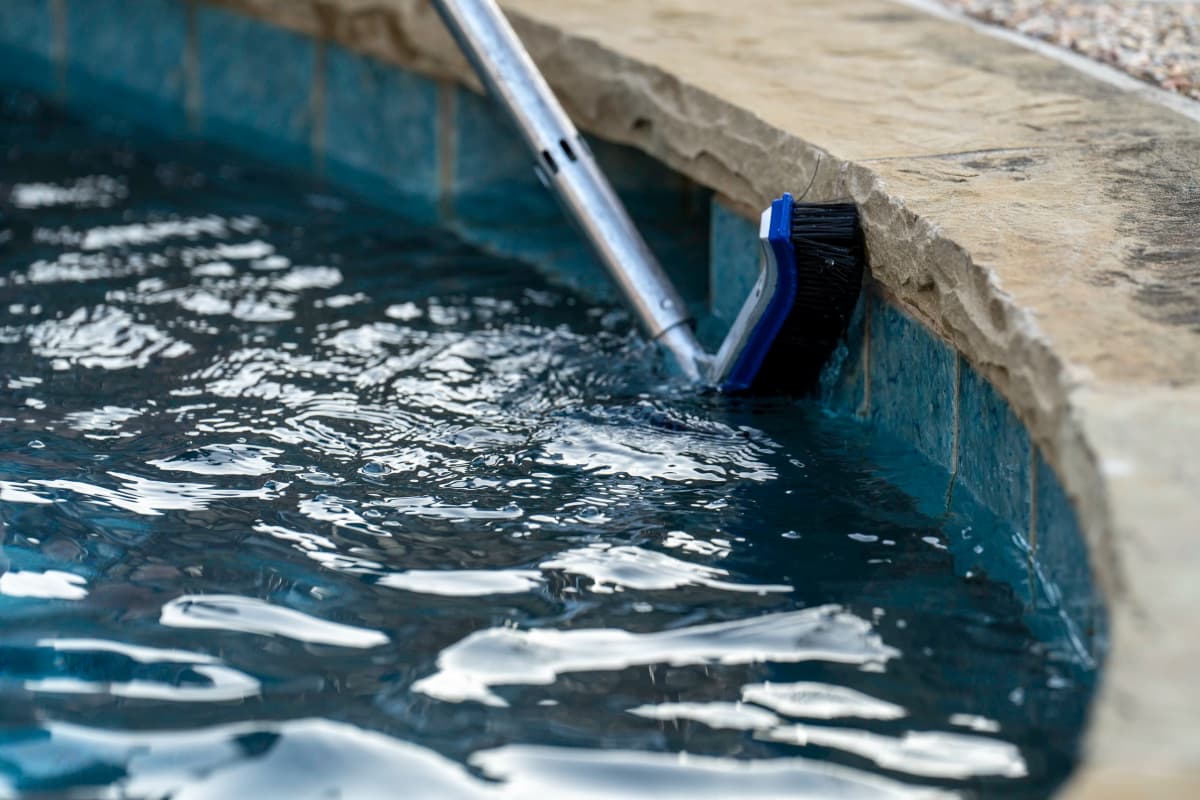 Pool technician brushing tile lines to prevent algae